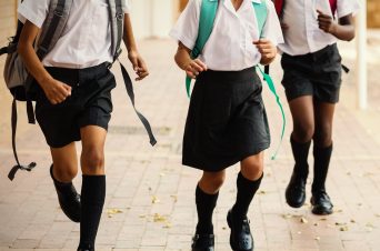 An image of three school children running down a corridor, holding backpacks.