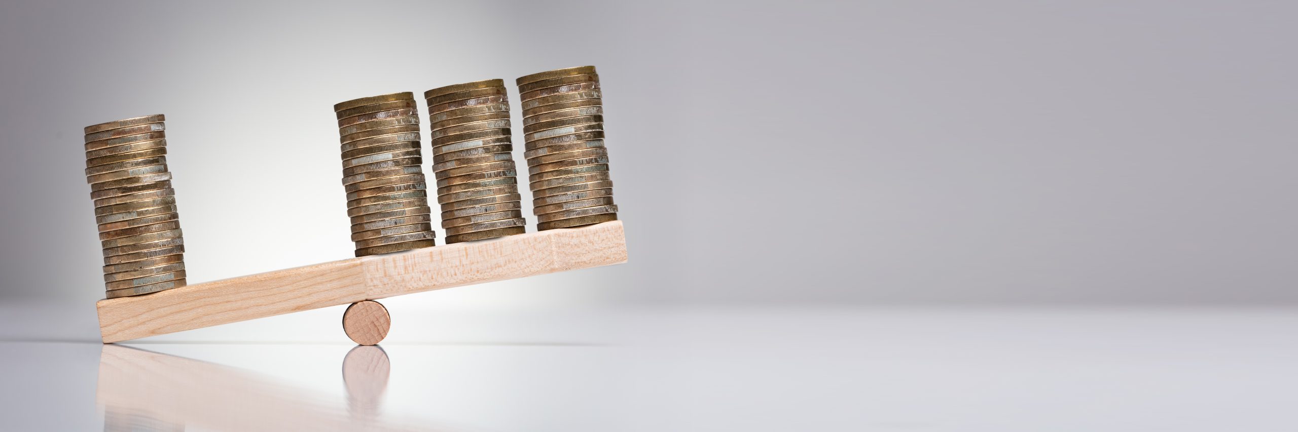 Stack Of Coins On Wooden Seesaw Over Gray Background