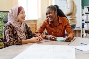 An image of two people sat at a table smiling.