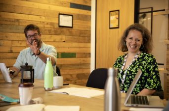 Joint Chief Execs of Innovation Unit, Matthew Horne and Sarah Gillinson, sat at a table in a wood panelled room smiling at the camera.