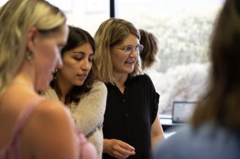 An image of three women looking at something conversationally.